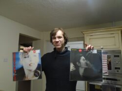 Oleg is holding up two vinyl records whilst stood in his kitchen