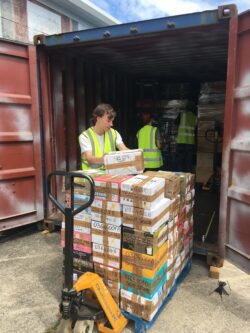 Volunteers Oleg and Alfiia are helping workshop manager Stuart to load the container with a pallet of cardboard boxes filled with haberdashery kits