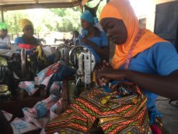 Three women sat at sewing machines making clothes with bright coloured fabric.